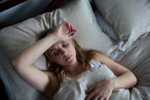 Mature woman lying awake in bed with one arm resting across her forehead.